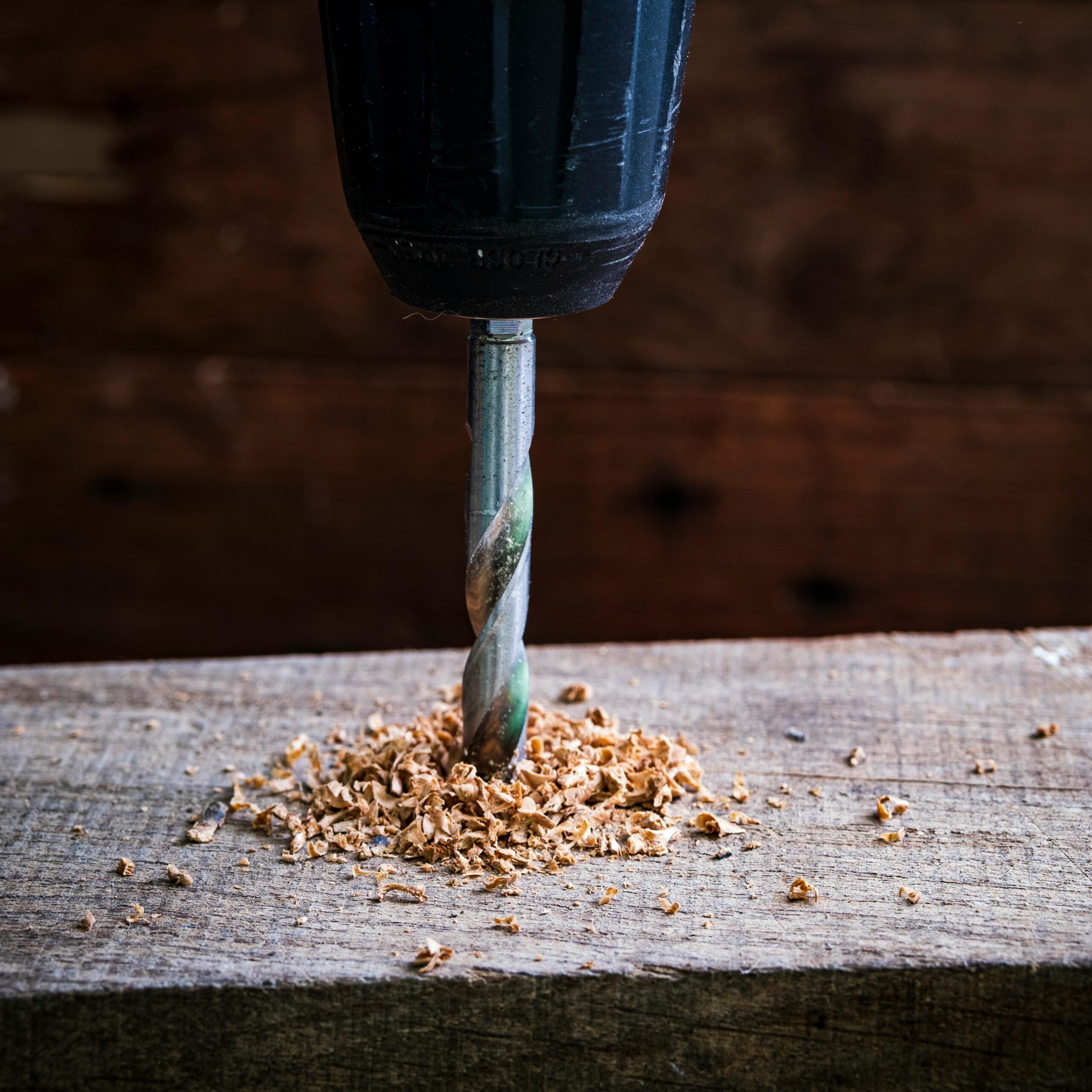 High-quality image of a drill bit boring into wood, creating sawdust on a rustic plank.